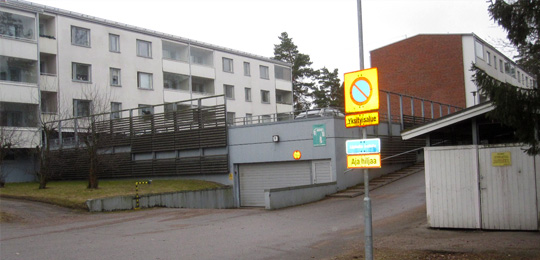 Sisäänkäynti Mellunhirven autotalliin ja sen päällä oleville autokansipaikoille. Oikealla jätekatos. Vas. talo 1 ja oikeassa reunassa talo 2:n pääty.