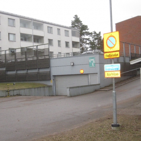 Sisäänkäynti Mellunhirven autotalliin ja sen päällä oleville autokansipaikoille. Oikealla jätekatos. Vas. talo 1 ja oikeassa reunassa talo 2:n pääty.